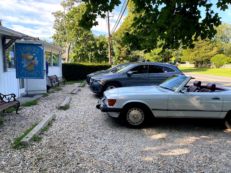 Weekend in The Hamptons: Parking lot with parked cars at Loaves and Fishes sign in East Hampton, New York